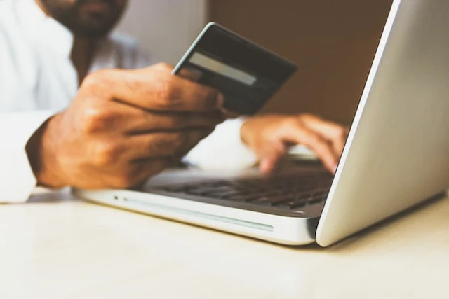 Seseorang yang menggunakan kartu kredit untuk melakukan pembayaran online di laptopnya